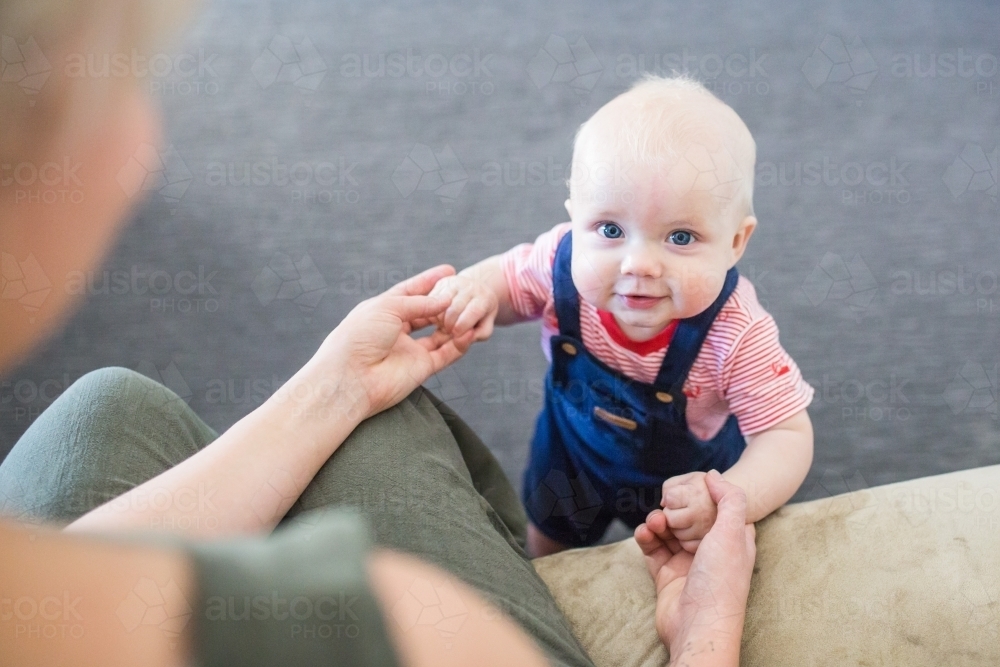 Mother holding hands of baby boy learning to walk - Australian Stock Image