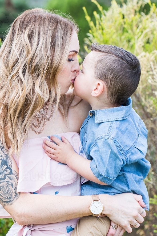 Mother holding mixed race aboriginal caucasian son on hip while they kiss - Australian Stock Image