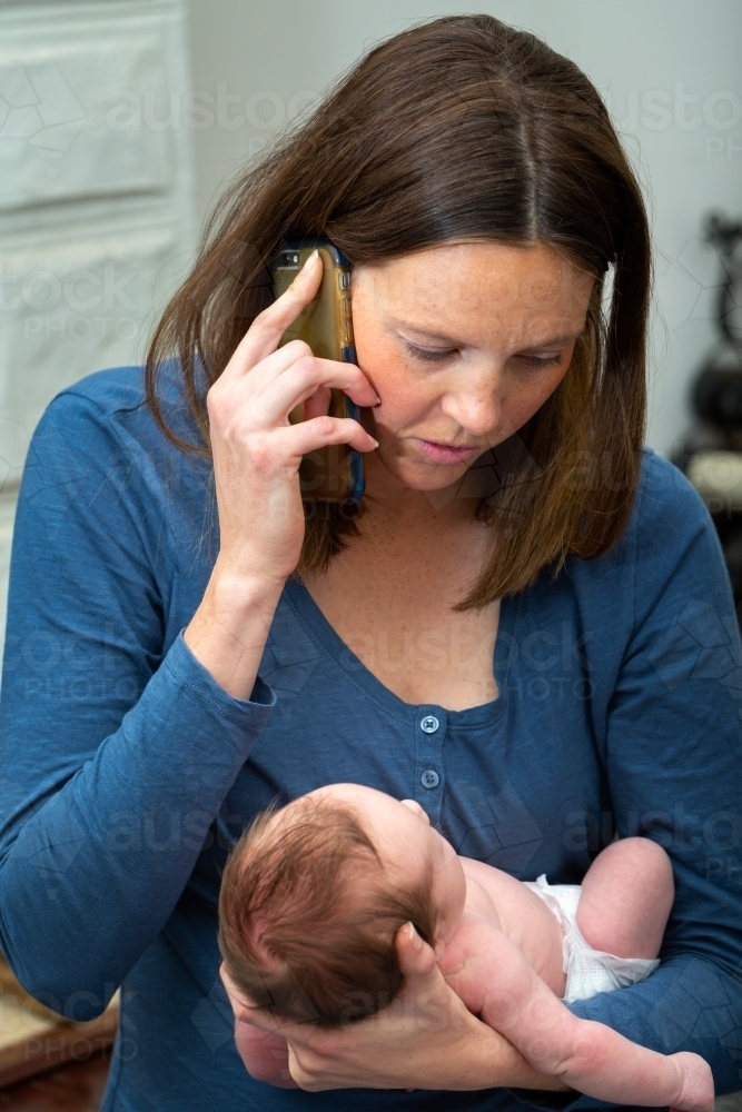 Mother holding newborn baby and talking on phone - Australian Stock Image