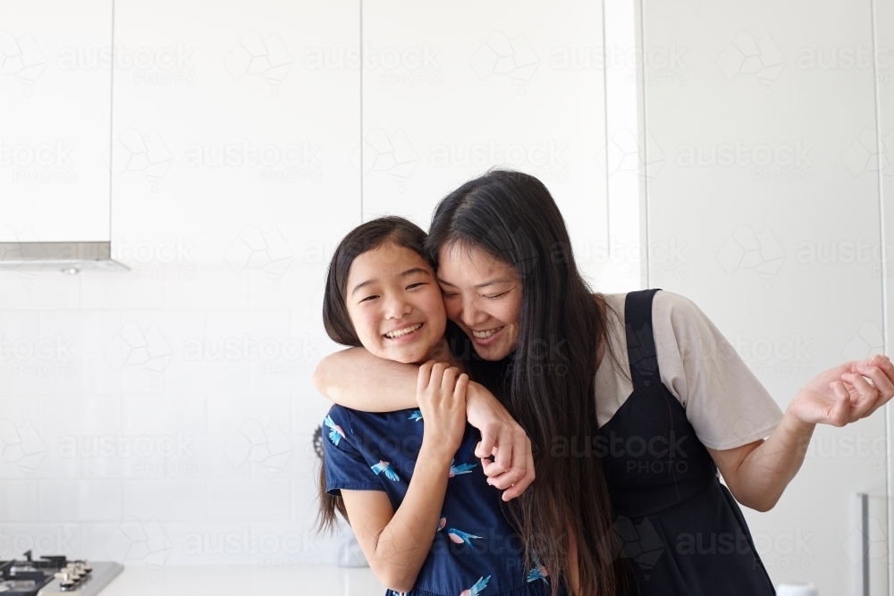 Mother hugging daughter in kitchen - Australian Stock Image