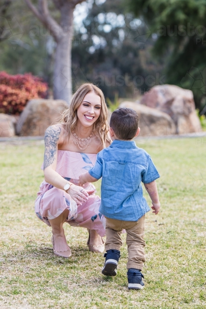 Mother kneeling down with arms outstretched to son running towards her - Australian Stock Image