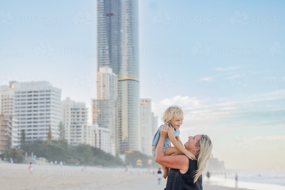 Mother lifting son in the air on Surfers Paradise beach with skyscrapers in background - Australian Stock Image