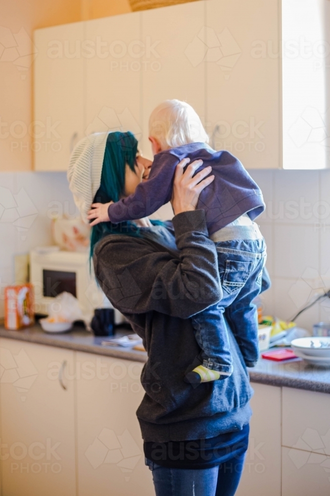 Mother lifting up child standing in kitchen - Australian Stock Image