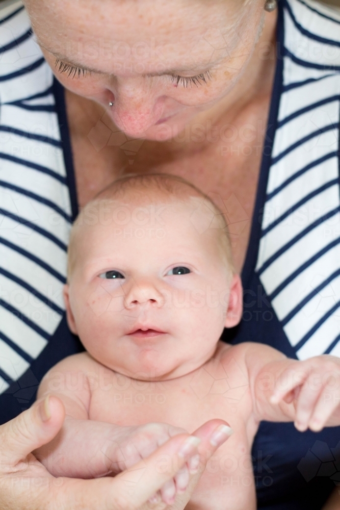 Mother looking down at newborn baby holding hands - Australian Stock Image