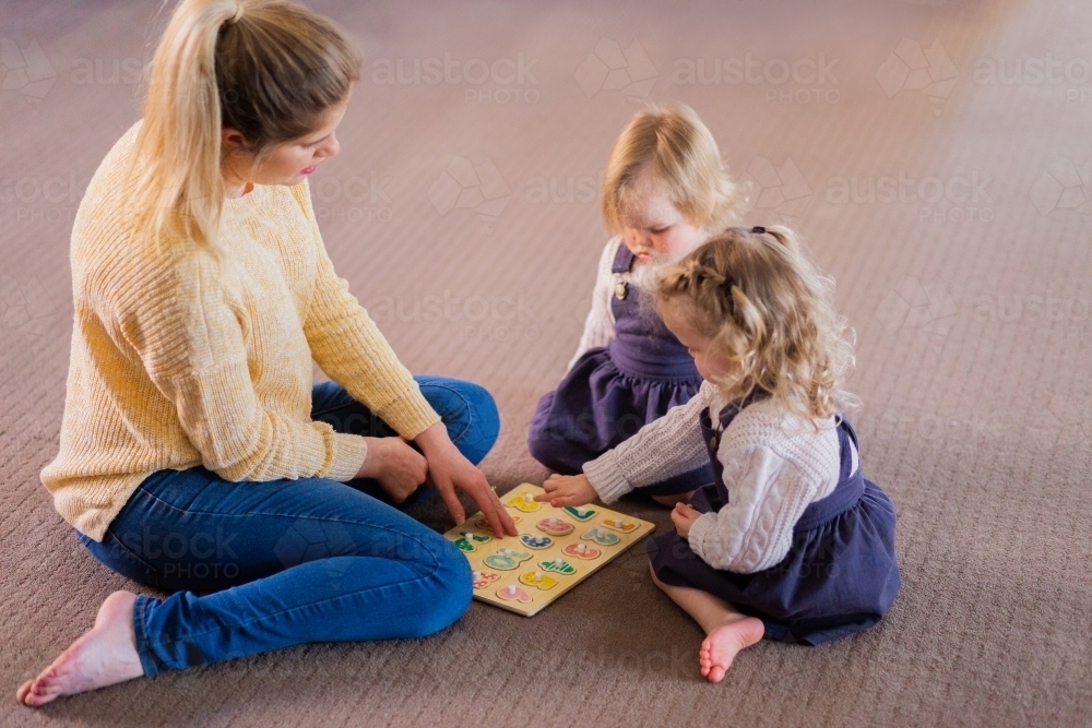 Mother sitting on floor with two children teaching them about numbers - Australian Stock Image