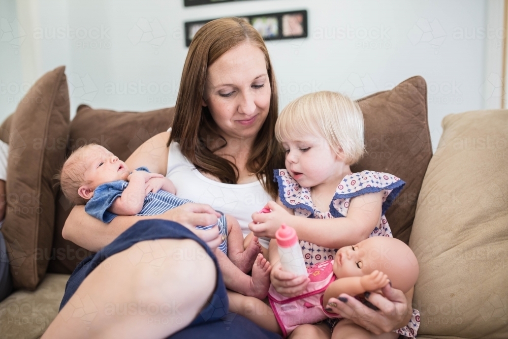 Mother sitting on lounge nursing newborn baby son while playing with daughter - Australian Stock Image