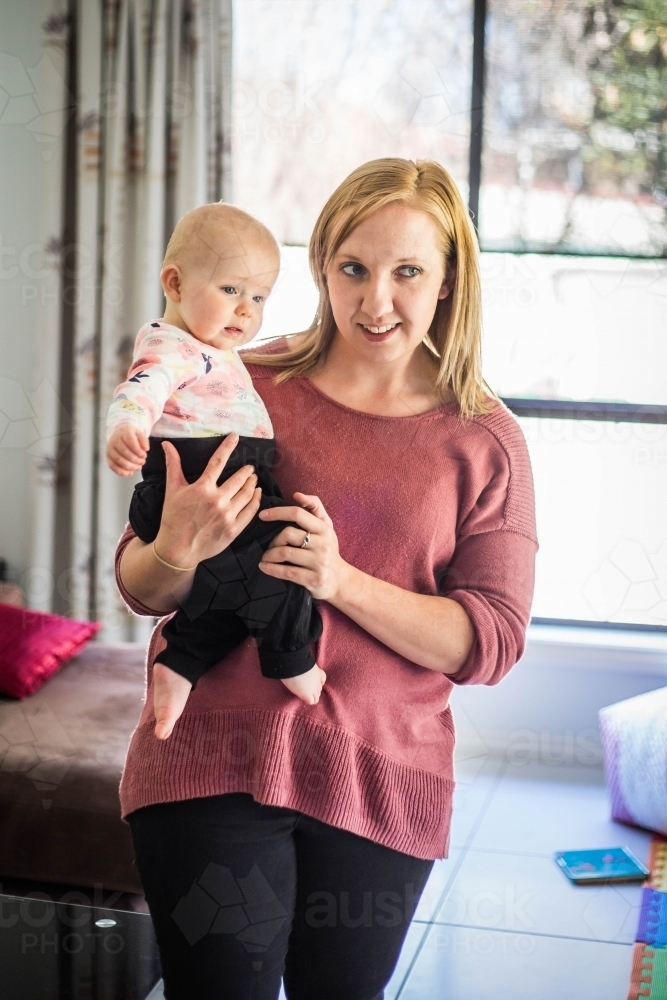 Mother standing holding baby in front of window - Australian Stock Image