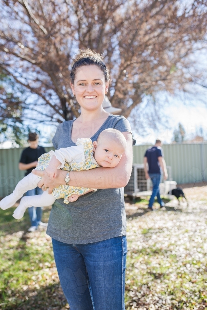 Mother standing in yard holding baby in arms - Australian Stock Image