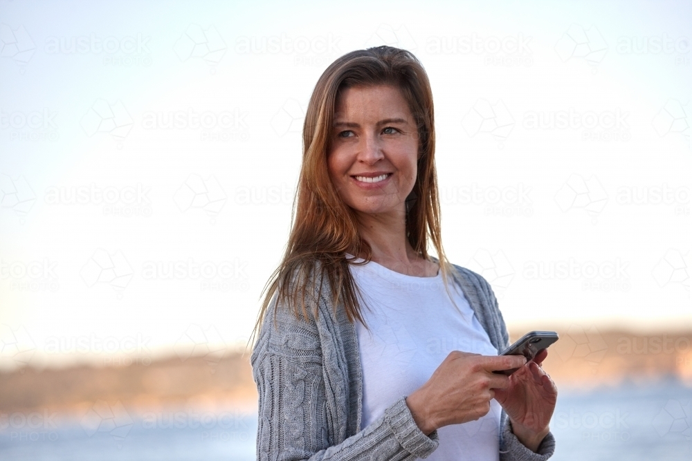 Mother using phone at seaside - Australian Stock Image