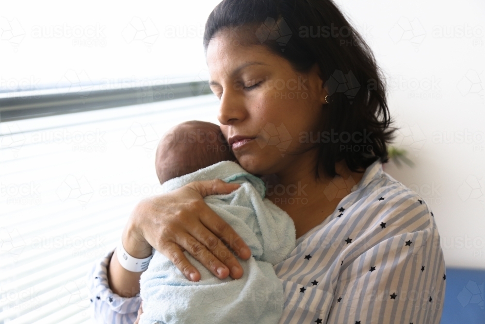 Mother with closed eyes, holding her new baby - Australian Stock Image