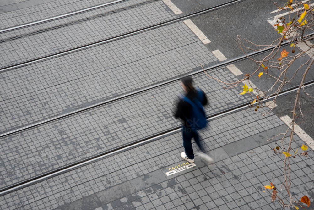 Motion blurred pedestrian crossing tram tracks seen from above - Australian Stock Image