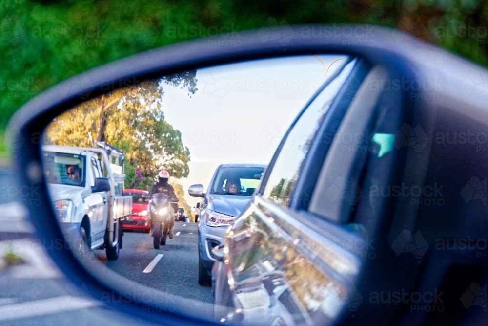 Motorbike rider coming up between cars in peak hour traffic - look out for motorbikes campaign - Australian Stock Image