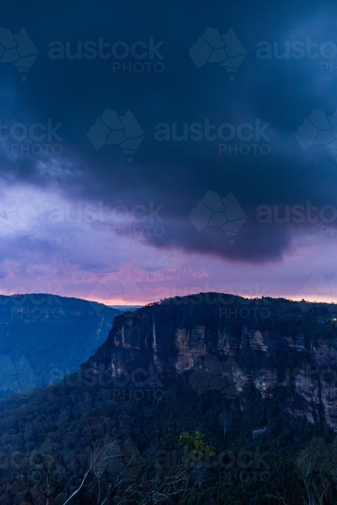 Mountain cliffs under pink and purple sunset sky with storm clouds - Australian Stock Image