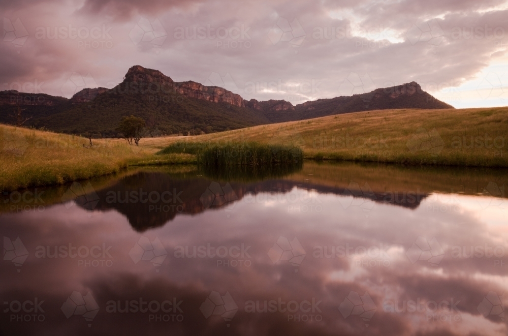 Mountain escarpment and sunset clouds reflected in farm dam - Australian Stock Image