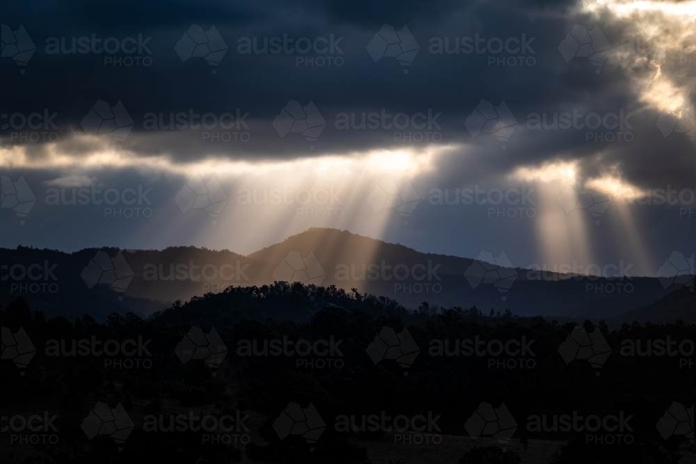 Mountains with sun rays piercing clouds at sunset - Australian Stock Image