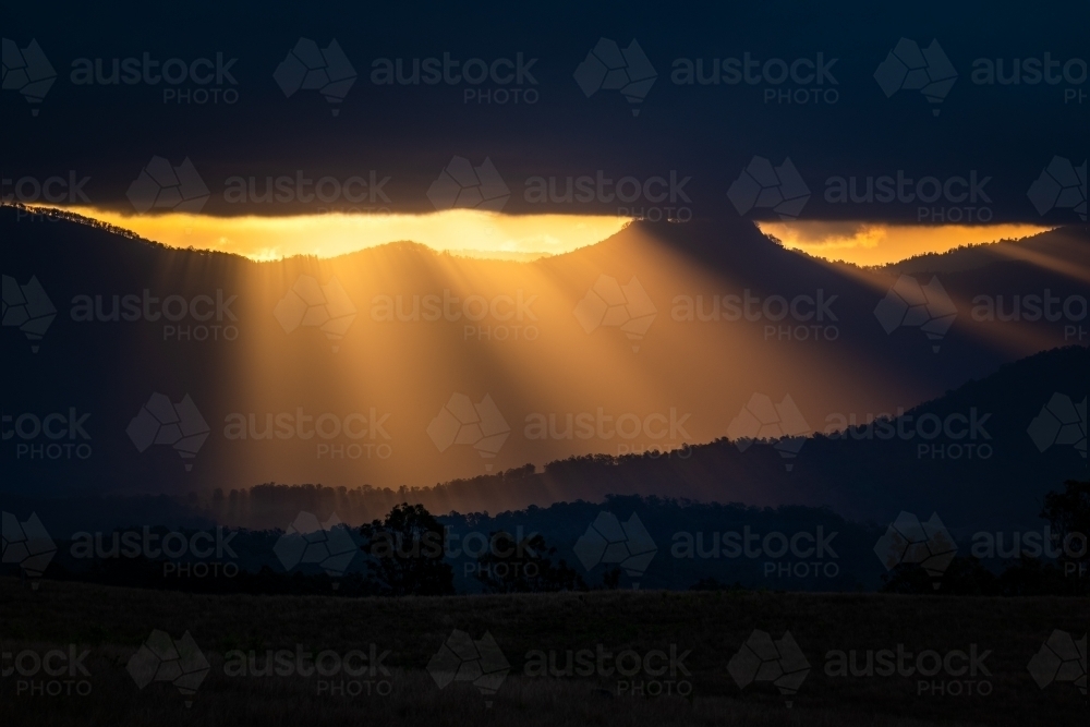 Mountains with sun rays piercing clouds at sunset - Australian Stock Image