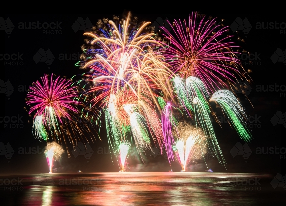 Multi coloured fireworks exploding over an ocean in the night sky. - Australian Stock Image