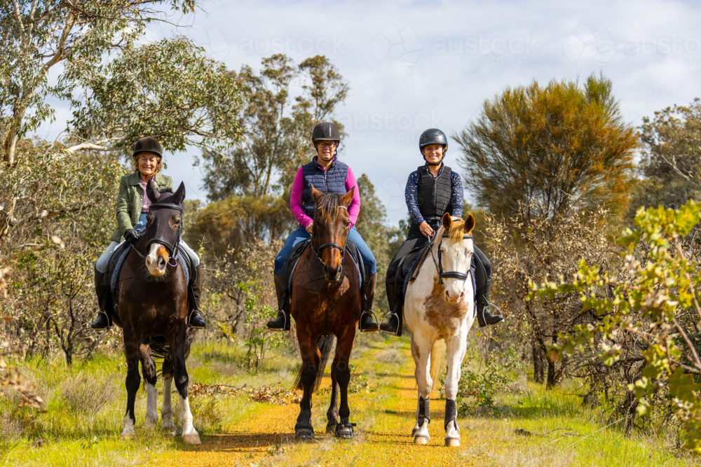Multi-generation women riding horses along a narrow dirt path. - Australian Stock Image
