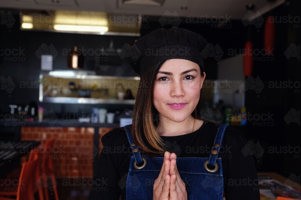 Multicultural Asian small business owner greeting in front of Thai restaurant - Australian Stock Image