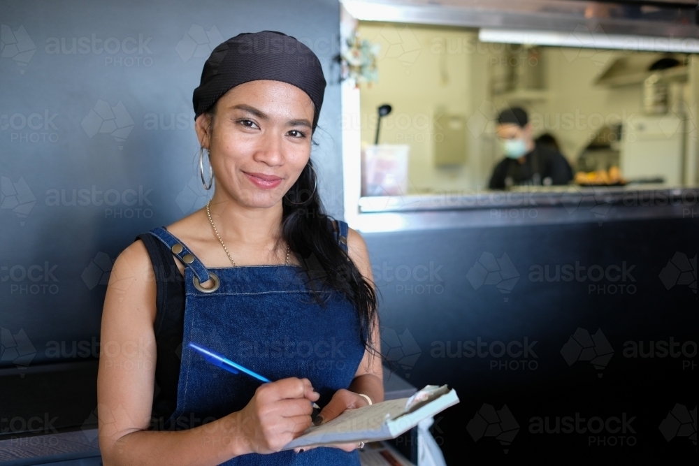 Multicultural Asian waitress taking order at Thai restaurant - Australian Stock Image