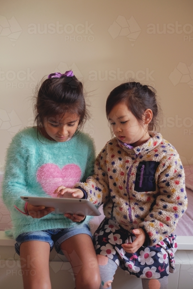 Multicultural kids using tablet in bedroom - Australian Stock Image