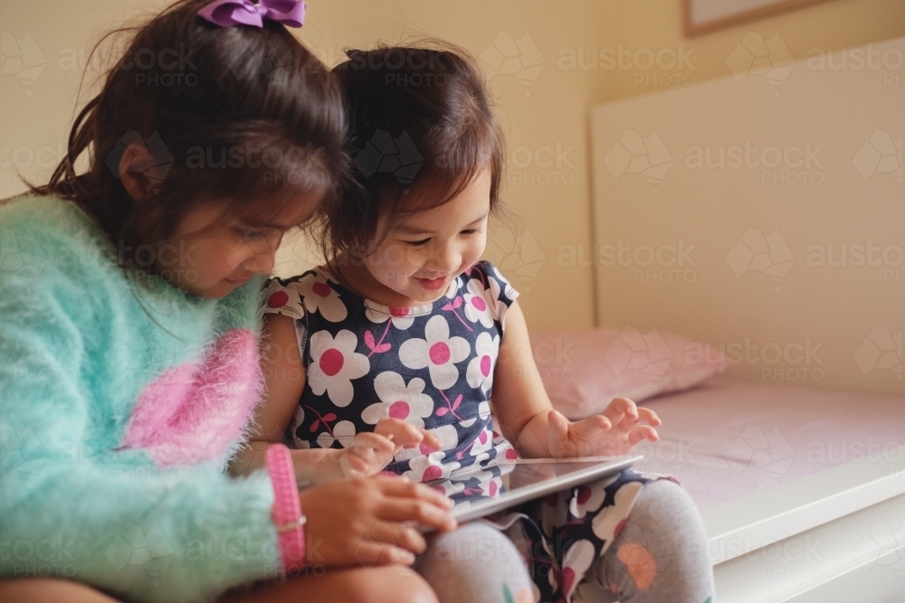 Multicultural kids using tablet in bedroom - Australian Stock Image