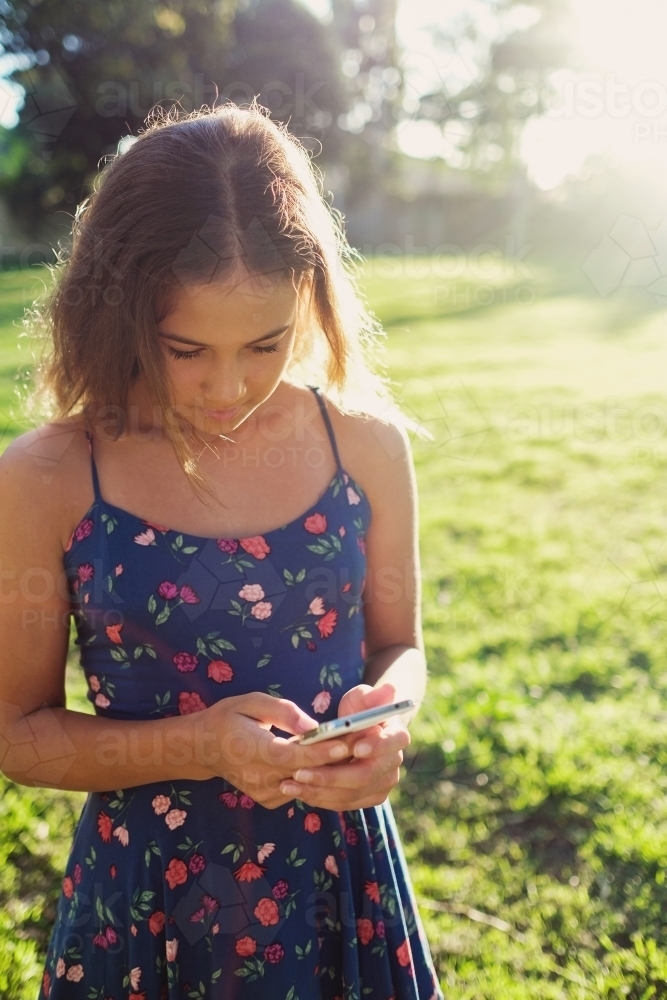 Multiethnic teenage girl using phone in the park - Australian Stock Image