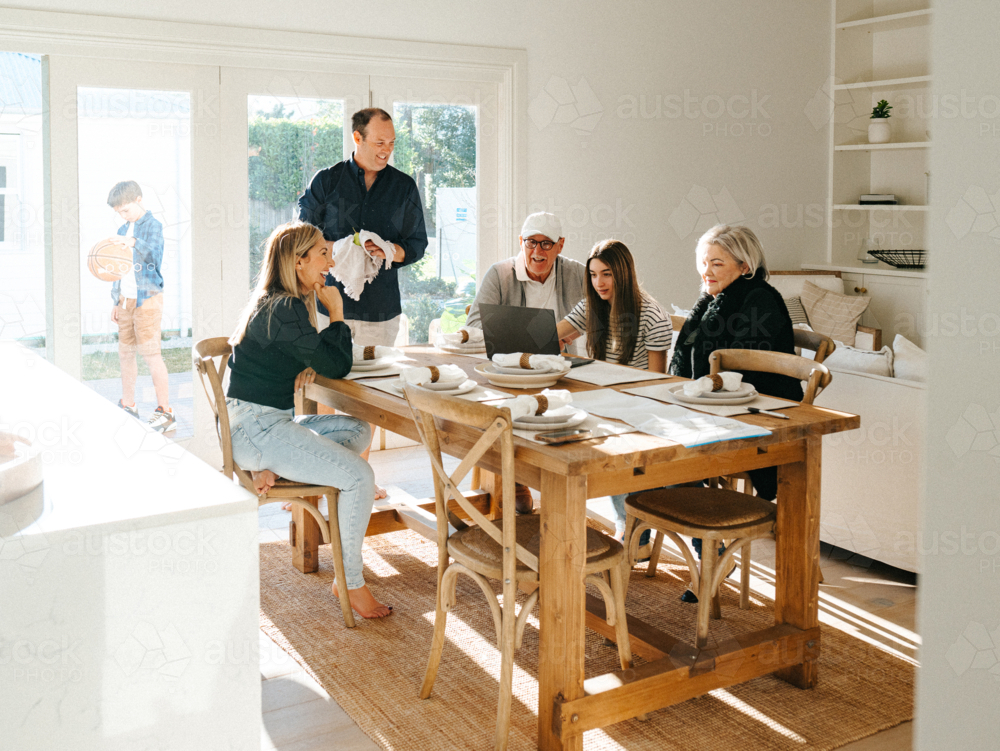 Multigeneration family gathered in the dining table while working on the computer. - Australian Stock Image