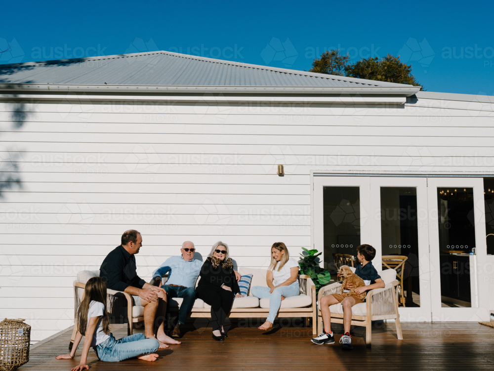 Multigeneration family sitting outside the wooden deck in the garden. - Australian Stock Image