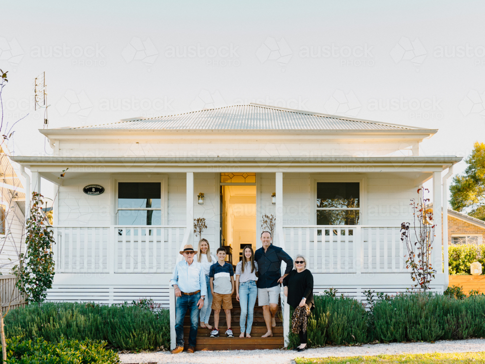 Multigeneration family standing on wooden steps of their porch in front of weatherboard home - Australian Stock Image