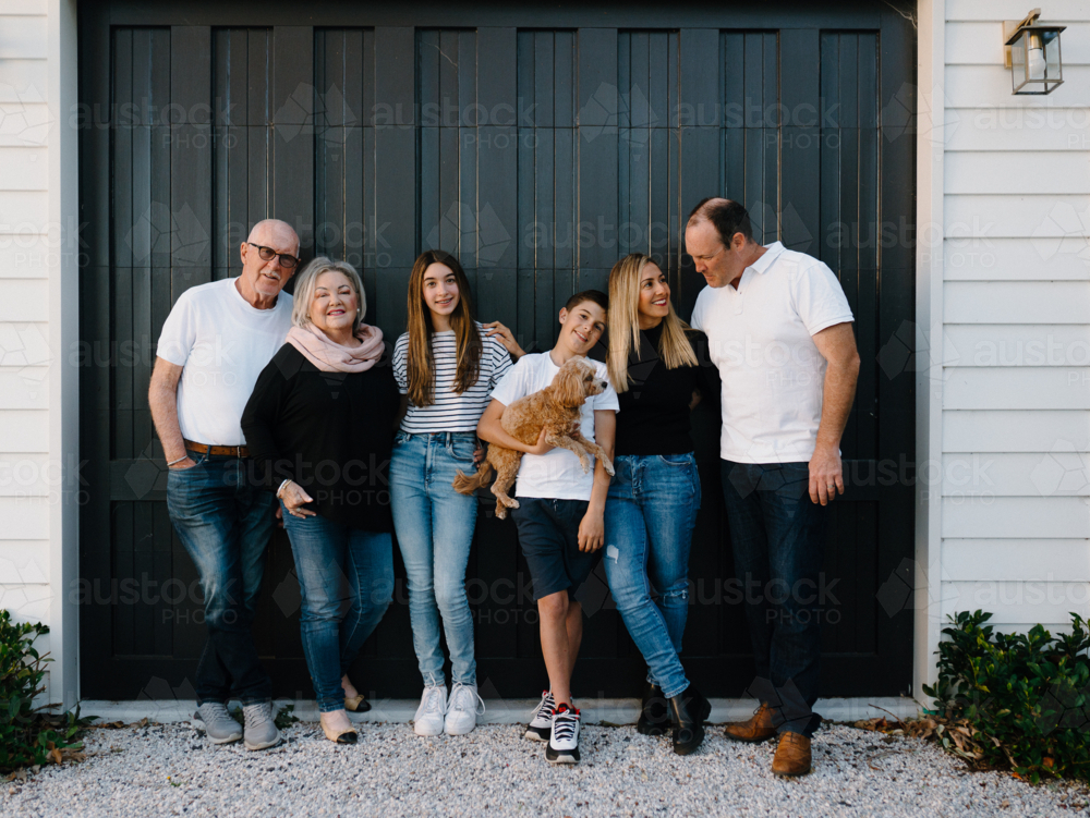 Multigenerational family standing outside in front of black garage door - Australian Stock Image