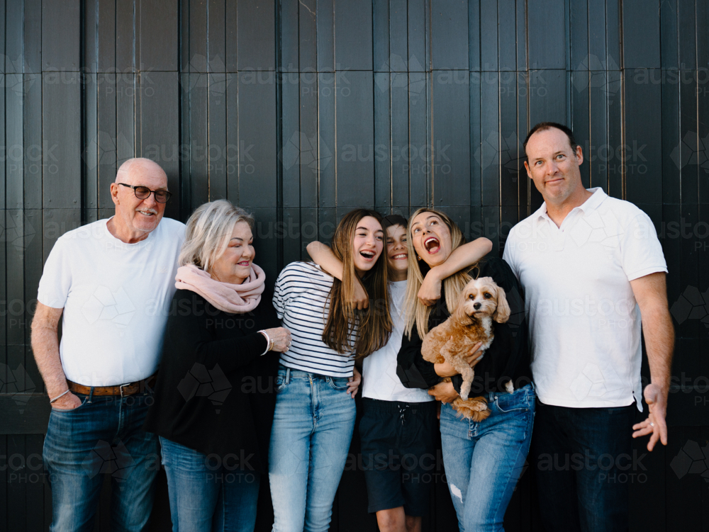 Multigenerational family standing outside in front of black garage door - Australian Stock Image