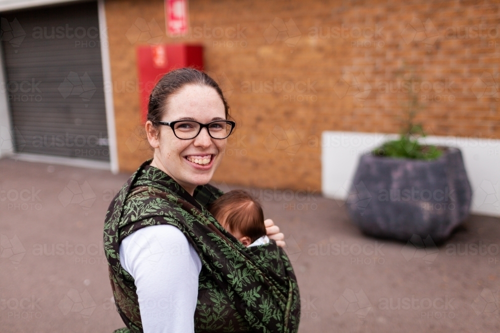 Mum holding baby in wrap carrier out and about down the street - Australian Stock Image