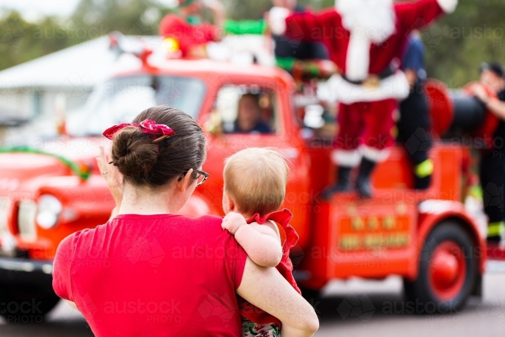 Mum holding baby to see the lolly run fire truck with Santa at Christmas time - Australian Stock Image