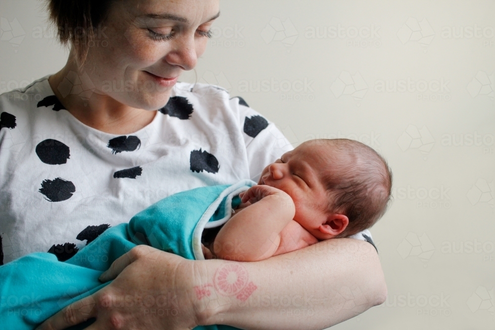 Mum holding her sleeping newborn, smiling - Australian Stock Image