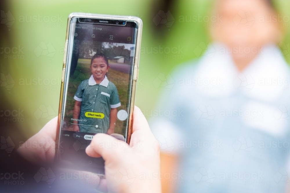 Mum holding mobile phone to take photos of her daughter on first day back to school - Australian Stock Image