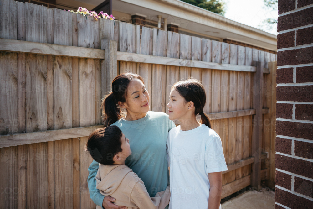 Mum hugging her children outside their house. - Australian Stock Image