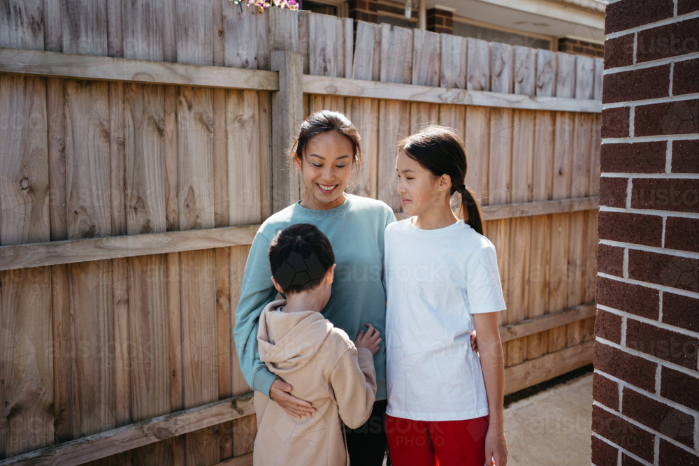 Mum hugging her children outside their house. - Australian Stock Image