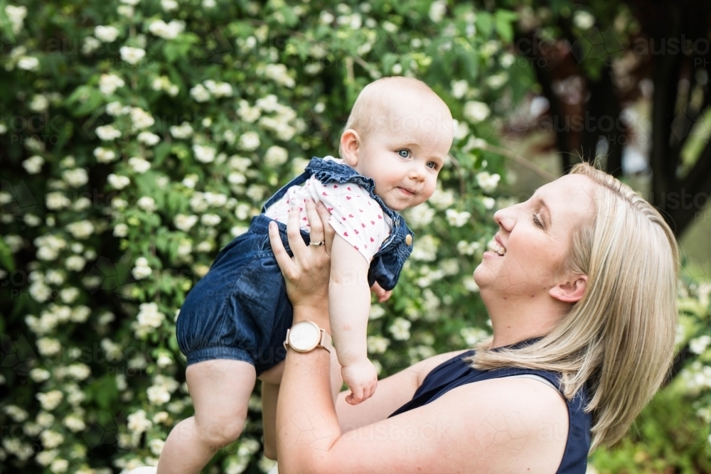 Mum looking at baby and smiling with flowers in background - Australian Stock Image