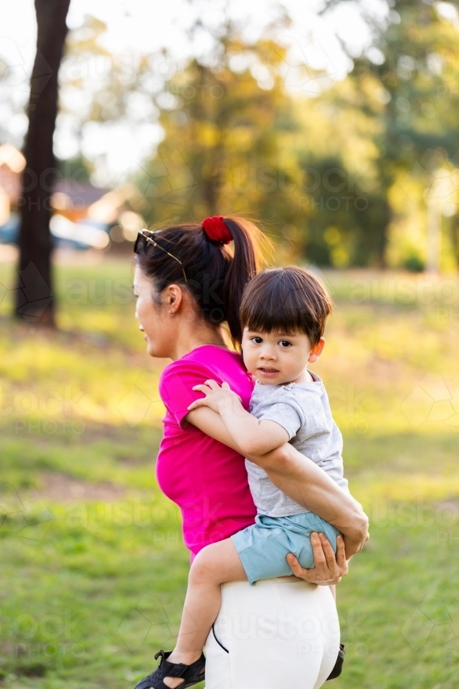 Mum of Asian ethnicity giving toddler piggyback ride in park - Australian Stock Image