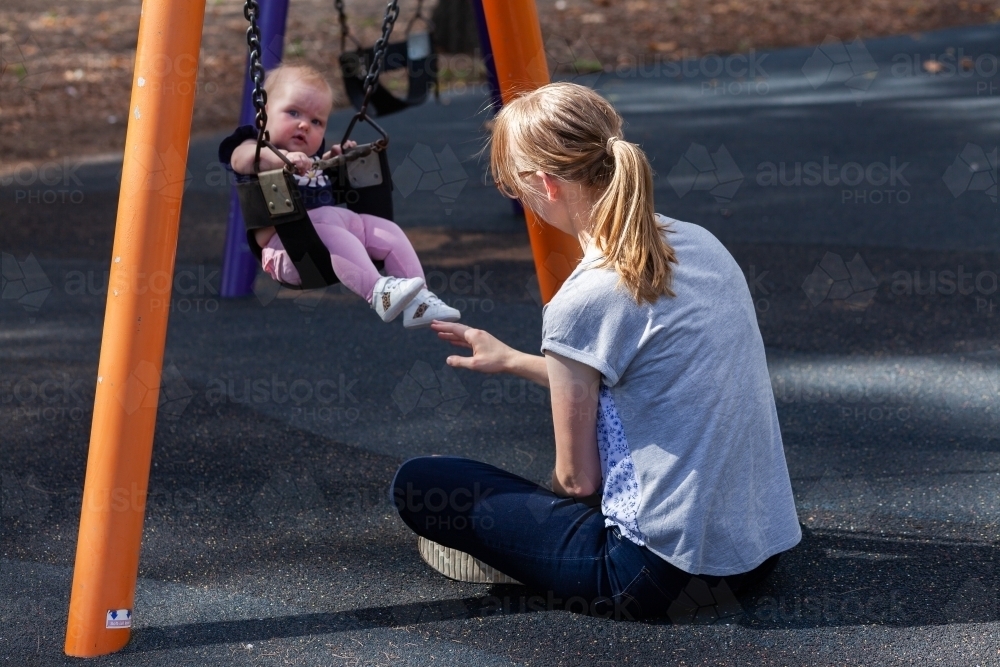 mum pushing baby on swing at park - Australian Stock Image