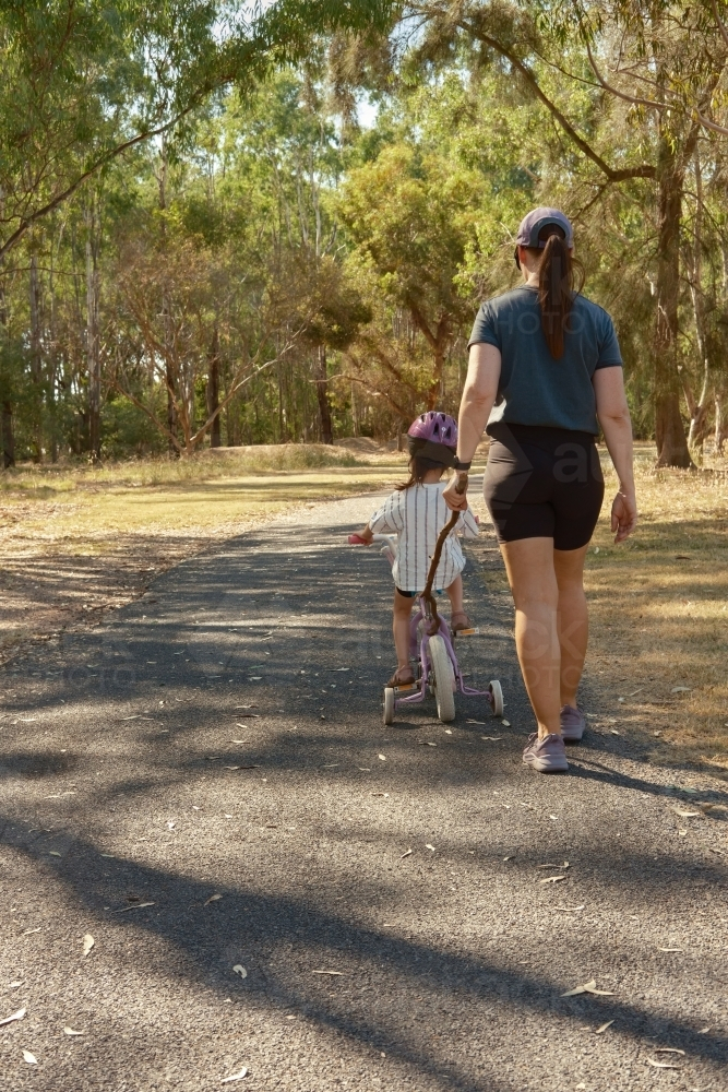 Mum walking little girl toddler on her bike on a bush track - Australian Stock Image