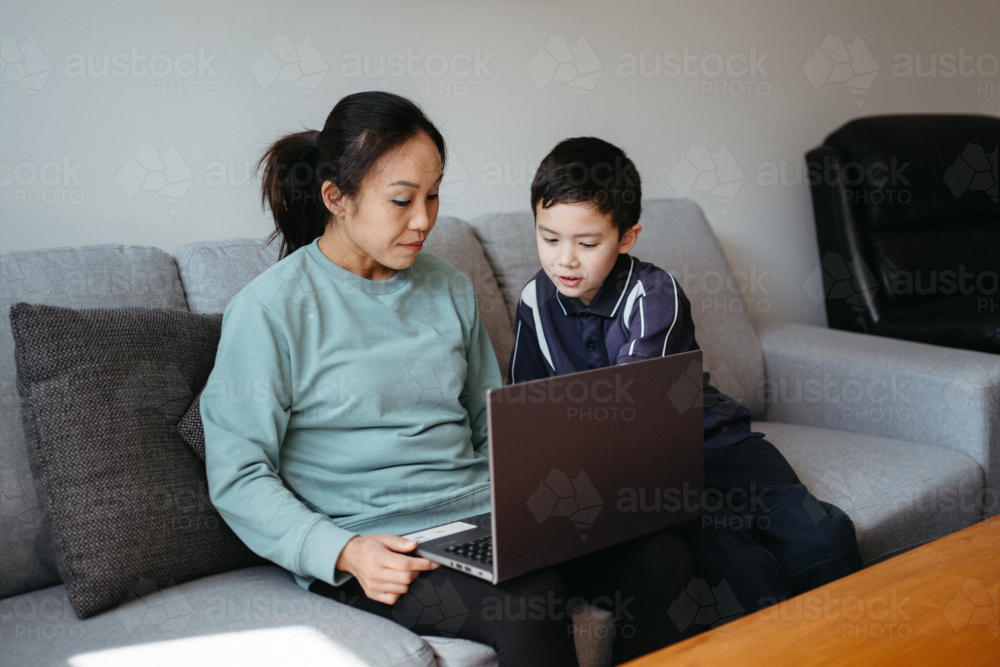 Mum working on her laptop on the couch with her kids. - Australian Stock Image