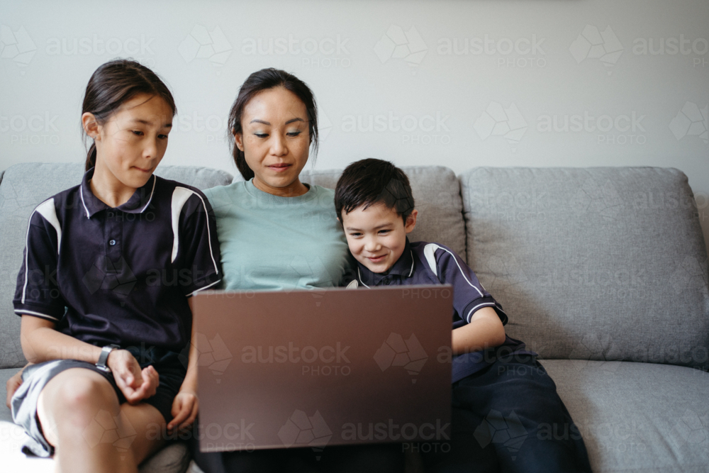 Mum working on her laptop on the couch with her kids. - Australian Stock Image