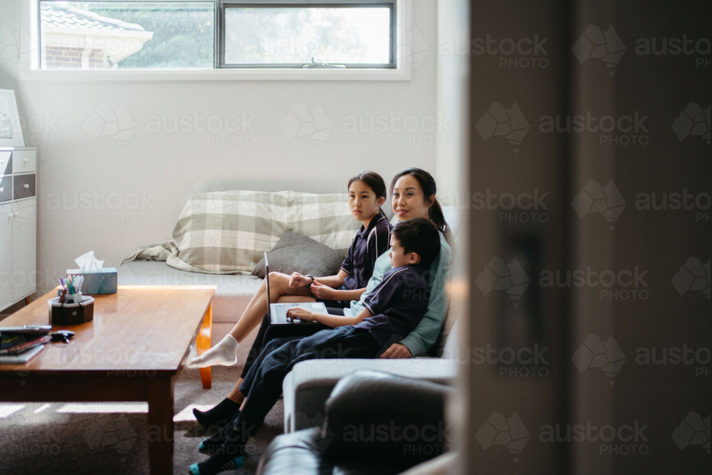 Mum working on her laptop on the couch with her kids. - Australian Stock Image