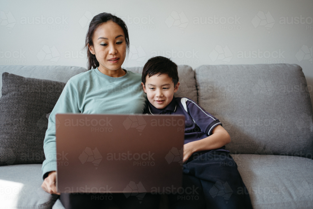 Mum working on her laptop with her son on the couch - Australian Stock Image