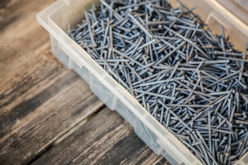 Nails in a container on wooden background - Australian Stock Image