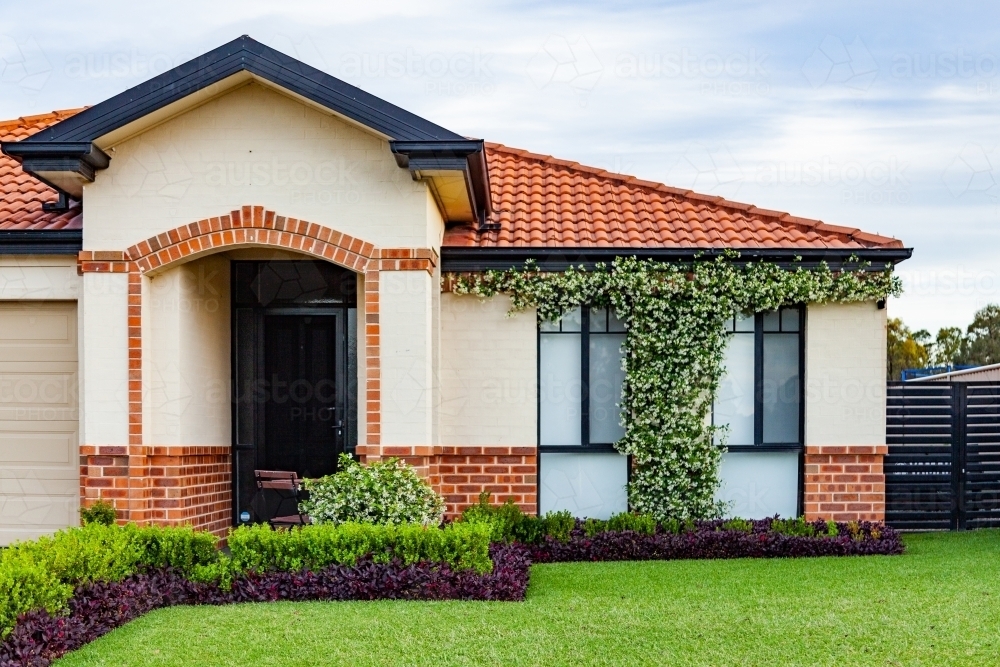 Neat house with ordered garden, lawn and vine growing on front of house - Australian Stock Image