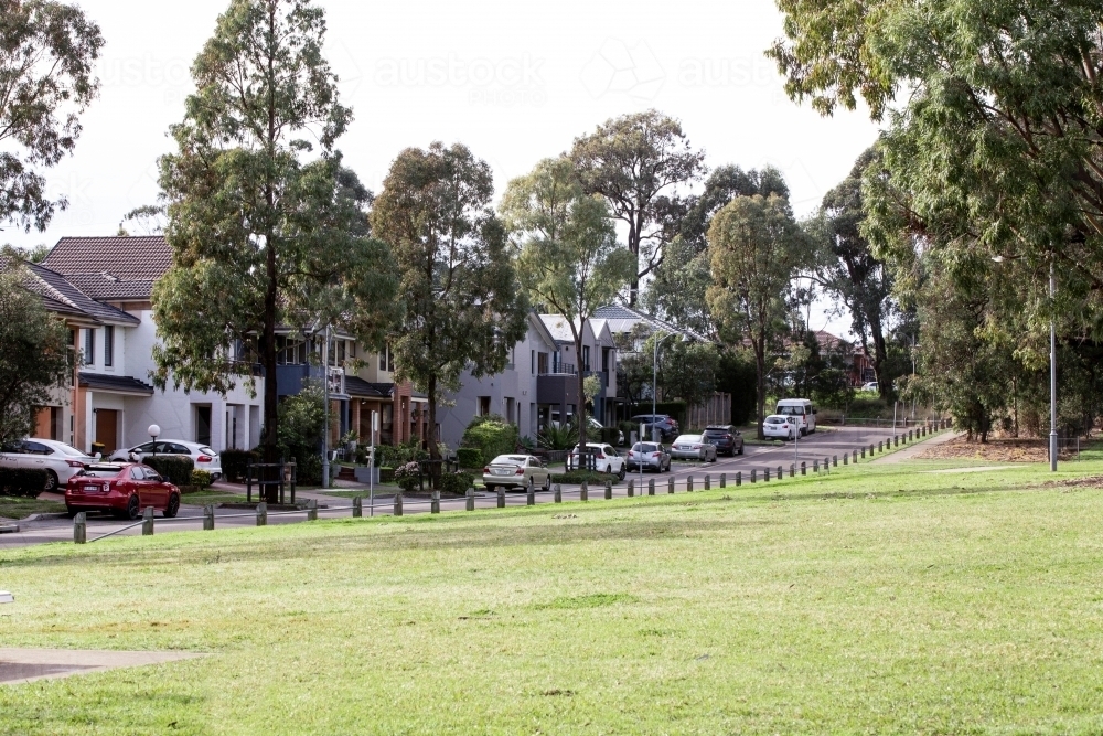 Neighbourhood with houses, trees and parked cars beside a park - Australian Stock Image