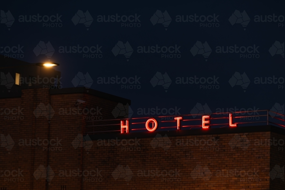 Neon Hotel sign illuminated on top of building at night time - Australian Stock Image